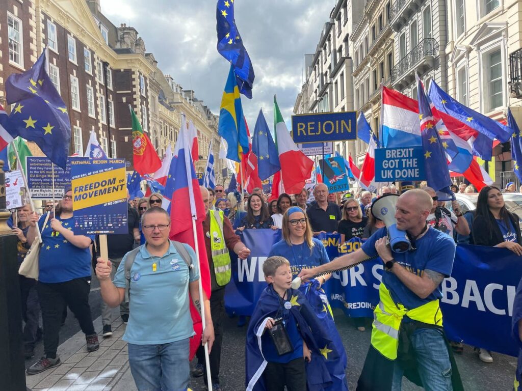 Pro-EU demonstrators rally in a European city, calling for the UK to rejoin the EU, amid political debates over Brexit and its impact on trade and policy.