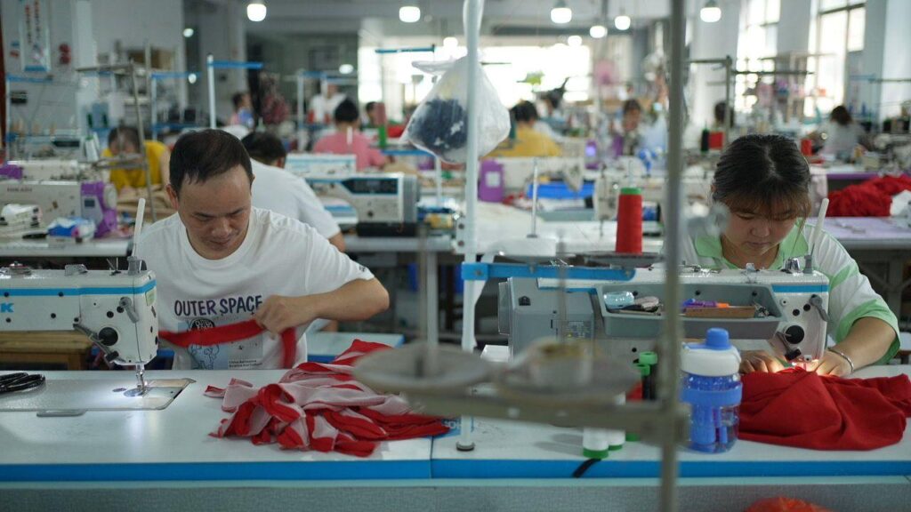 Workers in a Shein factory assemble garments under the glow of fluorescent lights, highlighting the labor behind Europe's low-cost fashion.