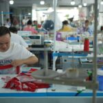 Workers in a Shein factory assemble garments under the glow of fluorescent lights, highlighting the labor behind Europe's low-cost fashion.