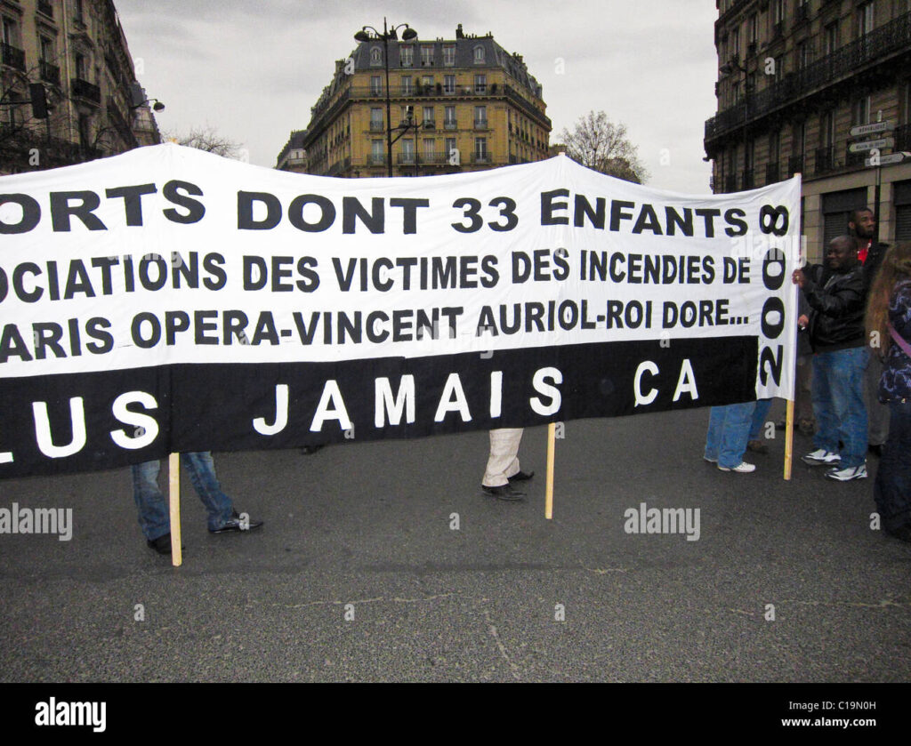 Protesters in Paris hold a banner demanding justice for victims of fires, highlighting the city's housing crisis and its parallels to the UK housing debate.